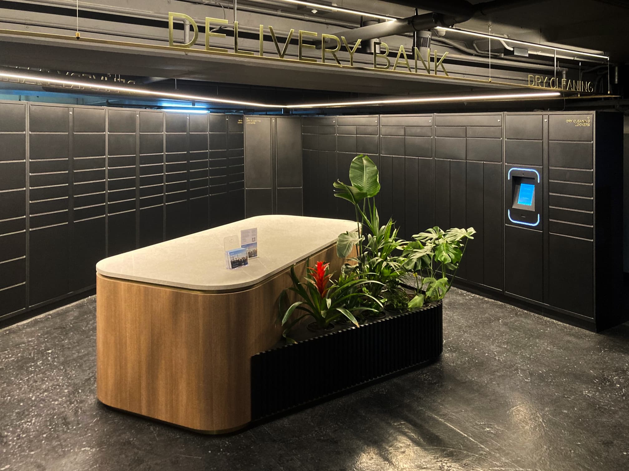 A modern parcel lockers for business station with a curved wooden counter and integrated planters, located in a dimly lit, gray tiled room.